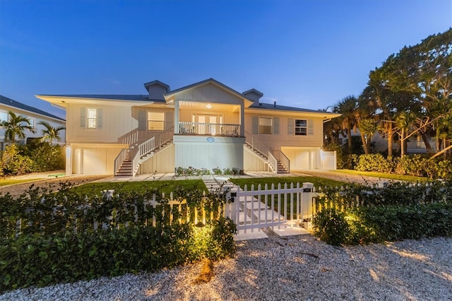 view of front of house featuring a gate, covered porch, stairs, a garage, and a fenced front yard