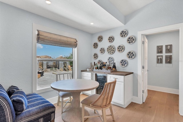 dining room with light wood finished floors, baseboards, beverage cooler, a dry bar, and recessed lighting