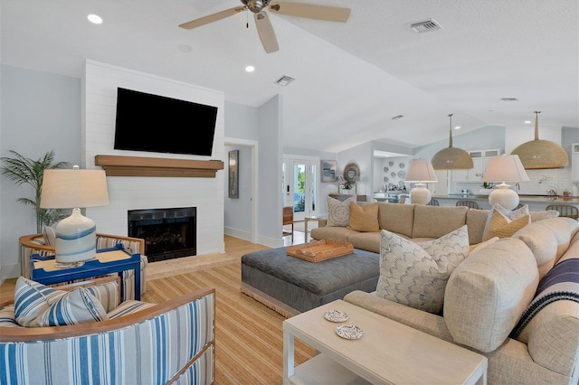 living area with visible vents, wood finished floors, a fireplace, and vaulted ceiling