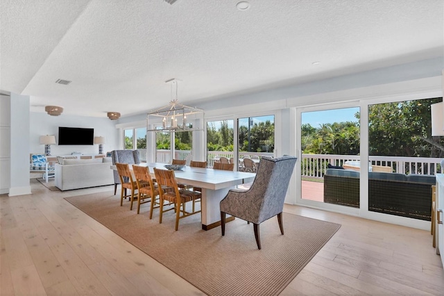 dining room featuring visible vents, light wood-style floors, an inviting chandelier, and a textured ceiling