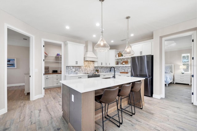 kitchen with open shelves, custom range hood, decorative backsplash, freestanding refrigerator, and a sink