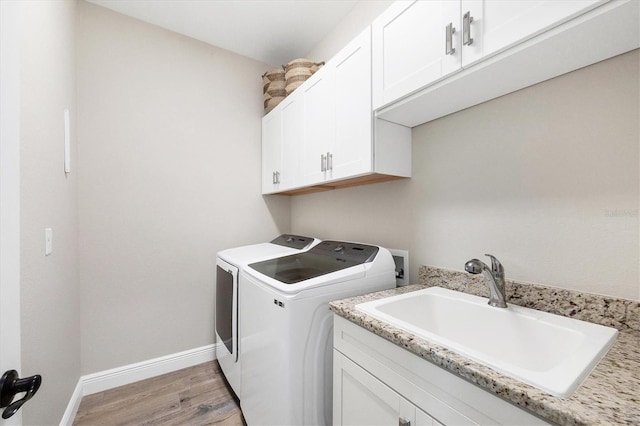 laundry area with baseboards, light wood finished floors, cabinet space, a sink, and washer and dryer