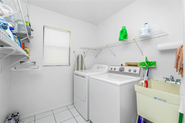 washroom featuring washing machine and clothes dryer, baseboards, light tile patterned floors, laundry area, and a sink