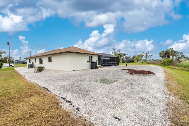 back of property featuring glass enclosure, central air condition unit, a lawn, and stucco siding