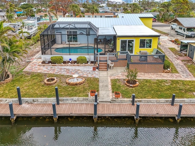 back of property featuring glass enclosure, a patio, a deck with water view, a yard, and an outdoor pool