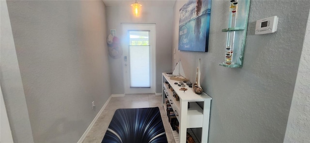 doorway with light tile patterned flooring, baseboards, and a textured wall