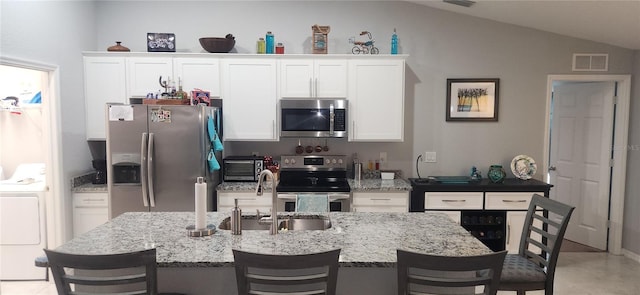 kitchen with a breakfast bar area, vaulted ceiling, stainless steel appliances, white cabinets, and washer / clothes dryer