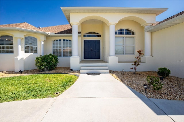 view of exterior entry with stucco siding and a shingled roof