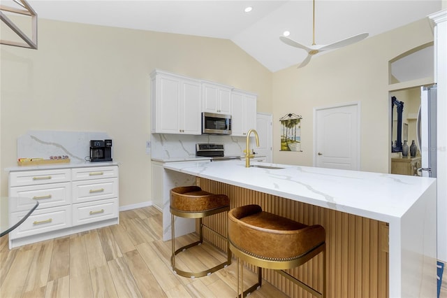 kitchen with lofted ceiling, decorative backsplash, stainless steel appliances, white cabinetry, and a sink