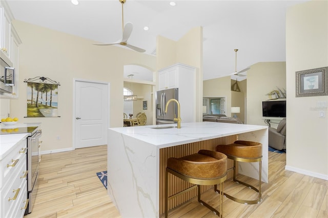 kitchen with stainless steel appliances, light wood-type flooring, a ceiling fan, and light stone countertops