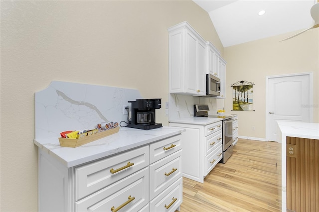 kitchen with stainless steel appliances, light wood-style floors, white cabinets, and vaulted ceiling