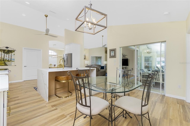 dining area featuring ceiling fan with notable chandelier, baseboards, light wood finished floors, and high vaulted ceiling