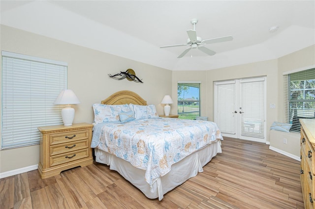 bedroom featuring light wood-style flooring, baseboards, a tray ceiling, and multiple windows