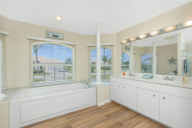 full bath featuring double vanity, a bath, wood finished floors, and a sink