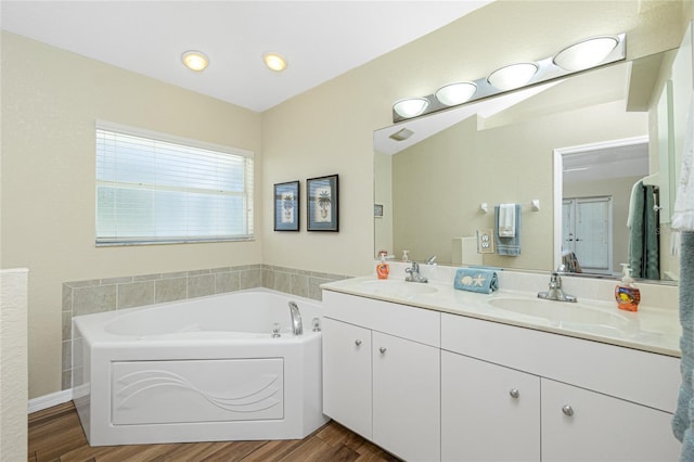 full bathroom with a bath, double vanity, wood finished floors, and a sink