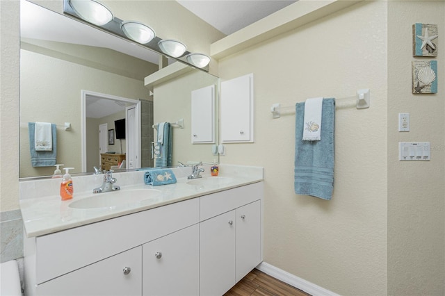 full bath featuring double vanity, wood finished floors, baseboards, and a sink