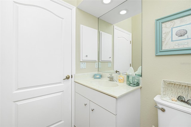 half bathroom featuring recessed lighting, toilet, and vanity