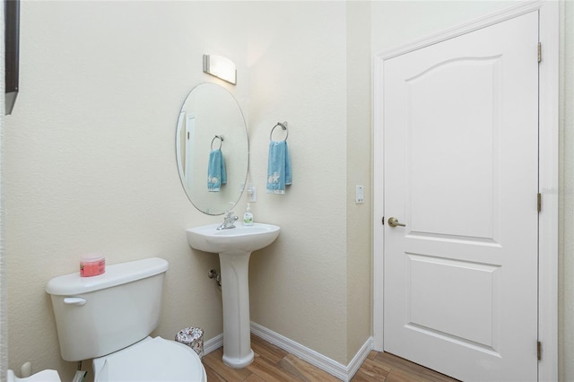 half bathroom with a sink, baseboards, toilet, and wood finished floors