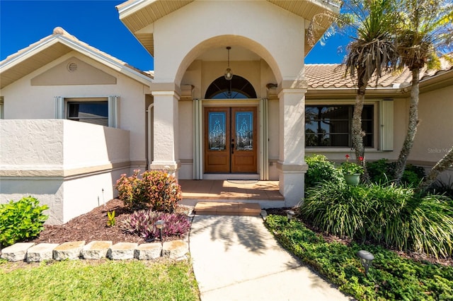 view of exterior entry with a tiled roof, french doors, and stucco siding