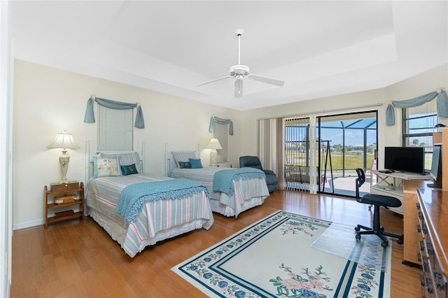 bedroom with wood finished floors, baseboards, a tray ceiling, ceiling fan, and access to exterior