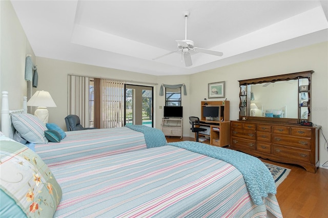 bedroom featuring access to exterior, a raised ceiling, a ceiling fan, and wood finished floors