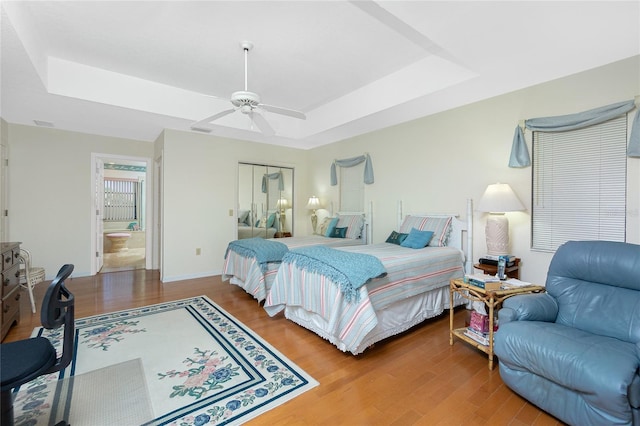 bedroom featuring connected bathroom, a raised ceiling, wood finished floors, and a ceiling fan