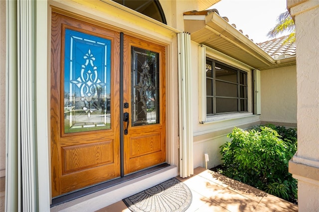 view of exterior entry with a tile roof and stucco siding