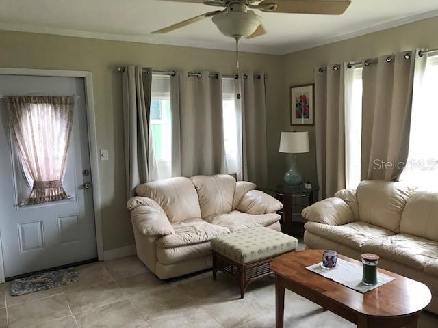 living room featuring crown molding, light tile patterned floors, a ceiling fan, and baseboards