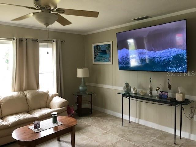 living room with visible vents, crown molding, and a ceiling fan