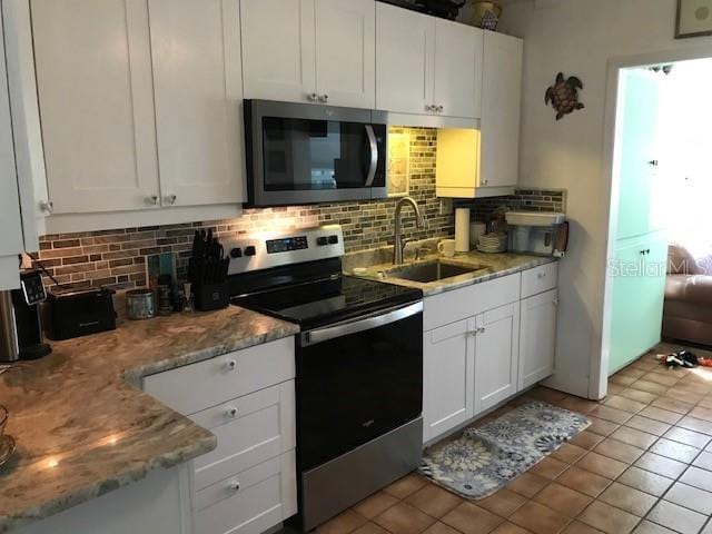 kitchen featuring a sink, white cabinetry, stainless steel appliances, light tile patterned flooring, and decorative backsplash