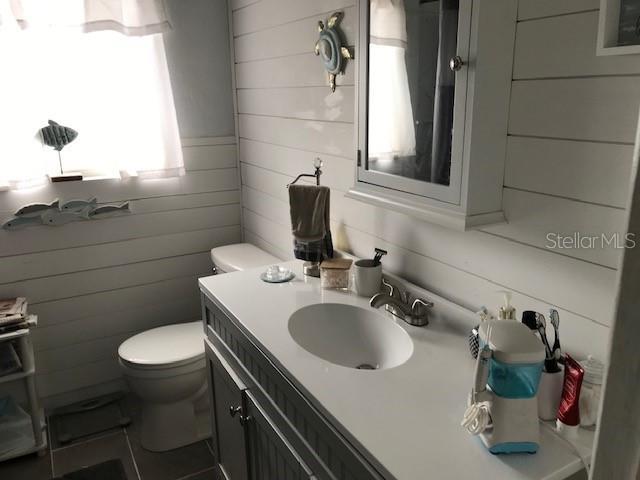 half bath with wooden walls, vanity, and toilet