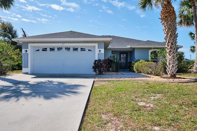 ranch-style home with a shingled roof, a front yard, stucco siding, a garage, and driveway