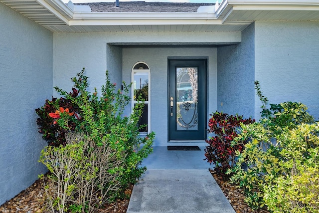 doorway to property featuring stucco siding and roof with shingles