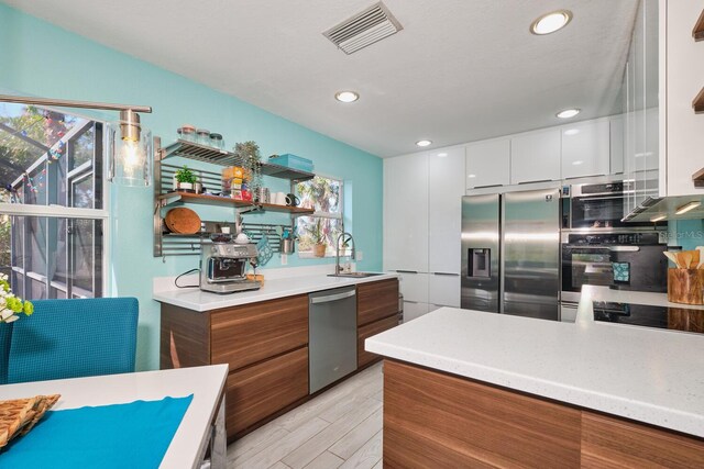 kitchen featuring visible vents, modern cabinets, a sink, appliances with stainless steel finishes, and brown cabinetry