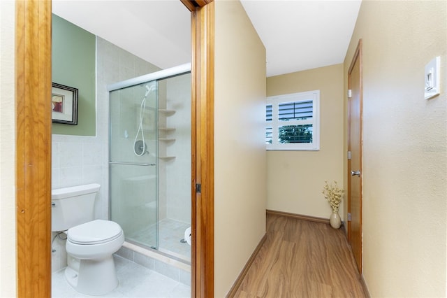 bathroom featuring toilet, tile walls, a shower stall, and tile patterned flooring