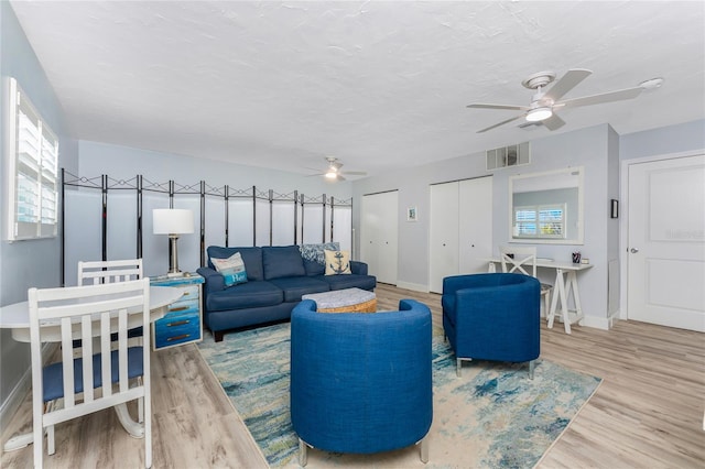 living room with baseboards, wood finished floors, visible vents, and ceiling fan