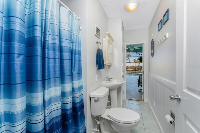 full bath featuring ceiling fan, tile patterned flooring, wainscoting, curtained shower, and toilet