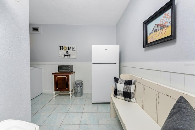 kitchen with light countertops, light tile patterned floors, a wainscoted wall, and freestanding refrigerator