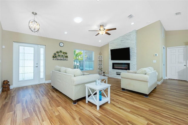 living room featuring visible vents, baseboards, lofted ceiling, a stone fireplace, and light wood-type flooring