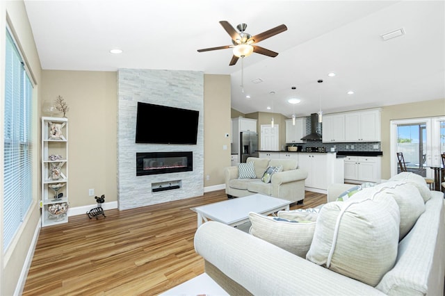 living area featuring a large fireplace, baseboards, ceiling fan, light wood-type flooring, and lofted ceiling