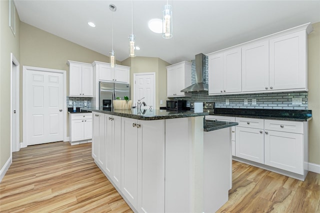 kitchen with a center island with sink, stainless steel fridge, light wood-style floors, white cabinets, and wall chimney range hood