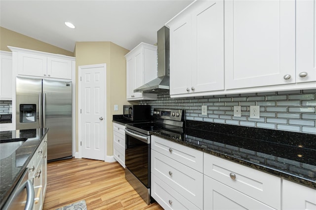 kitchen featuring light wood-style flooring, appliances with stainless steel finishes, white cabinetry, wall chimney range hood, and backsplash