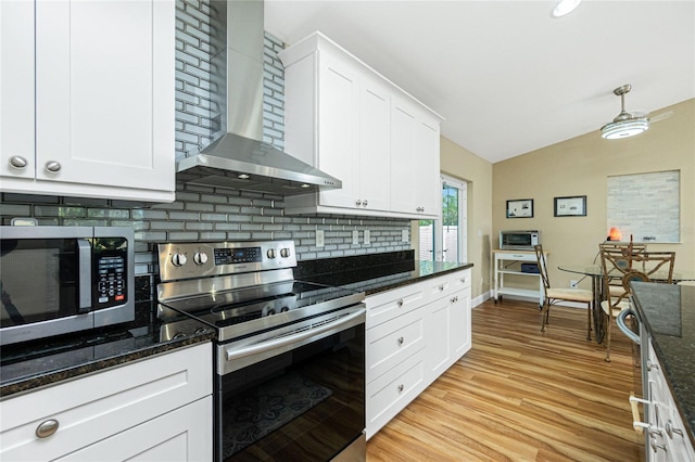 kitchen featuring light wood finished floors, tasteful backsplash, wall chimney range hood, stainless steel appliances, and white cabinetry