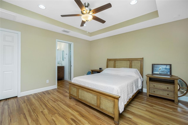 bedroom with visible vents, baseboards, light wood-type flooring, and a tray ceiling