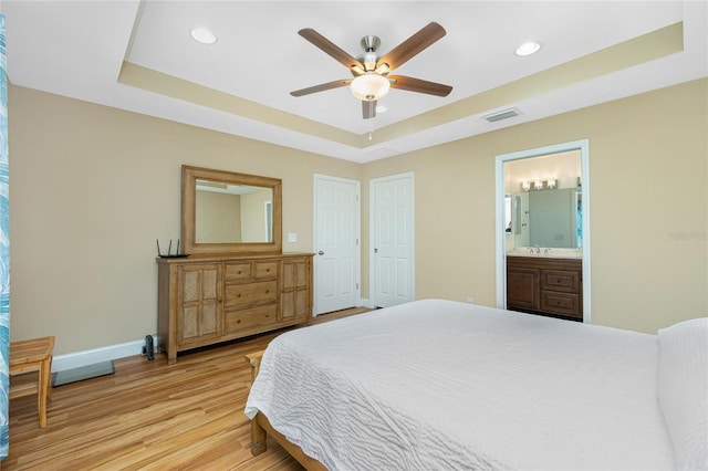 bedroom featuring a tray ceiling, baseboards, light wood-style floors, and visible vents