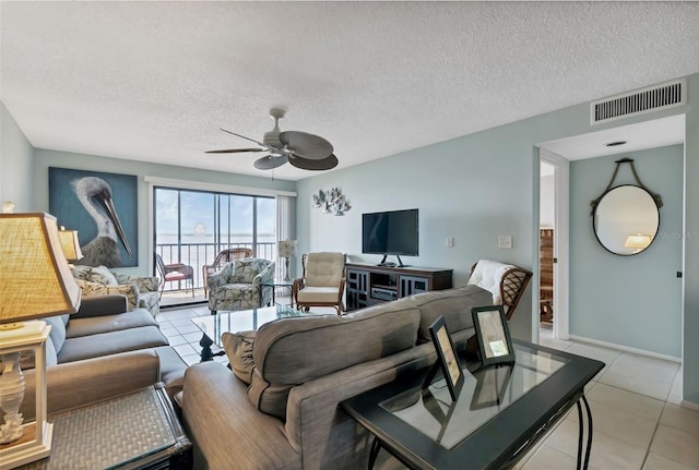 living room featuring light tile patterned floors, visible vents, a textured ceiling, and a ceiling fan