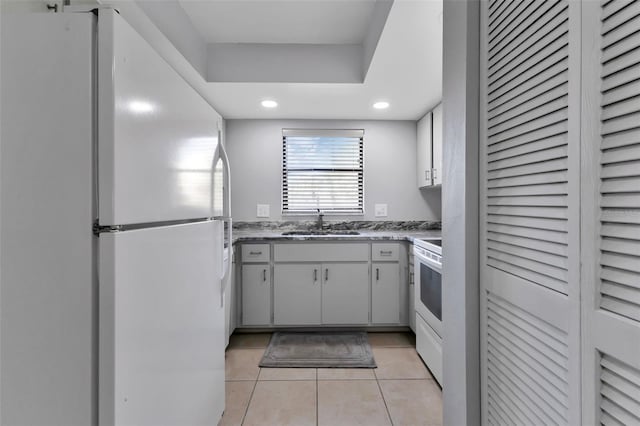 kitchen with a sink, light stone counters, recessed lighting, white appliances, and light tile patterned floors