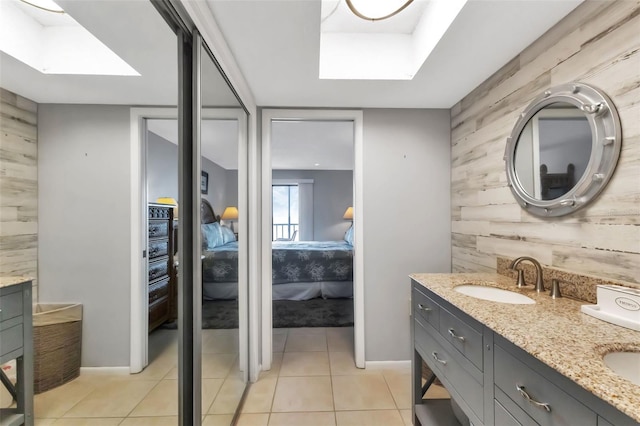 full bath featuring double vanity, a skylight, a sink, tile patterned floors, and connected bathroom