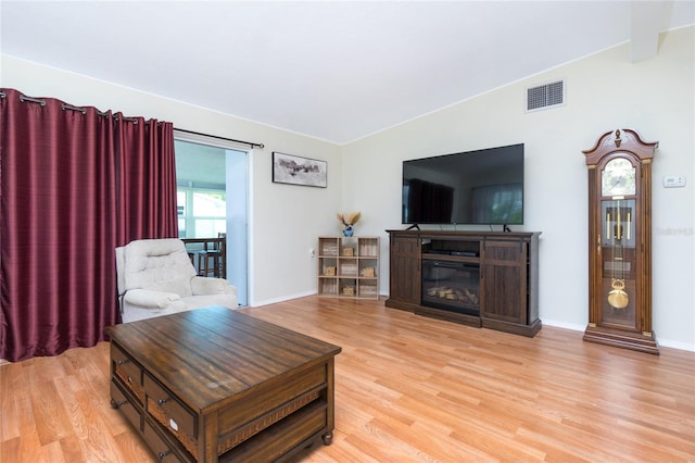 living room with a glass covered fireplace, baseboards, visible vents, and light wood-type flooring