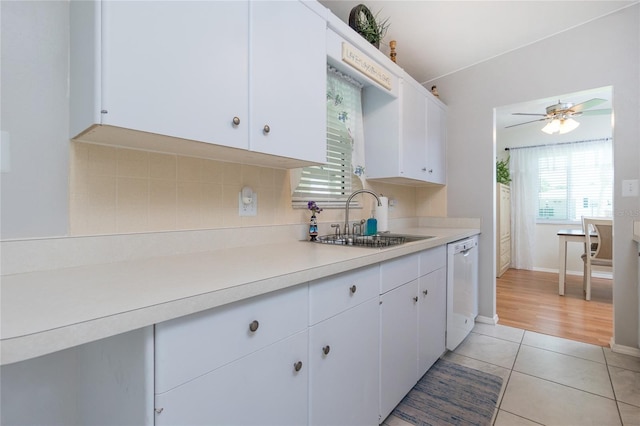 kitchen featuring light countertops, white cabinets, white dishwasher, and a sink